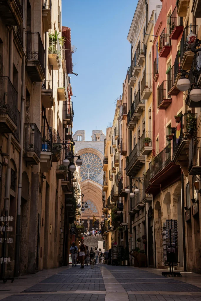 Street view of Tarragona's Cathedral rose window, framed by colorful historic buildings and bustling pedestrians.