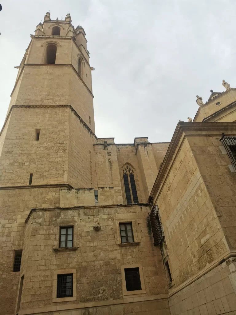 View of the bell tower and façade of the Prioral Sant Pere Church in Reus, showcasing Gothic architecture under a cloudy sky.